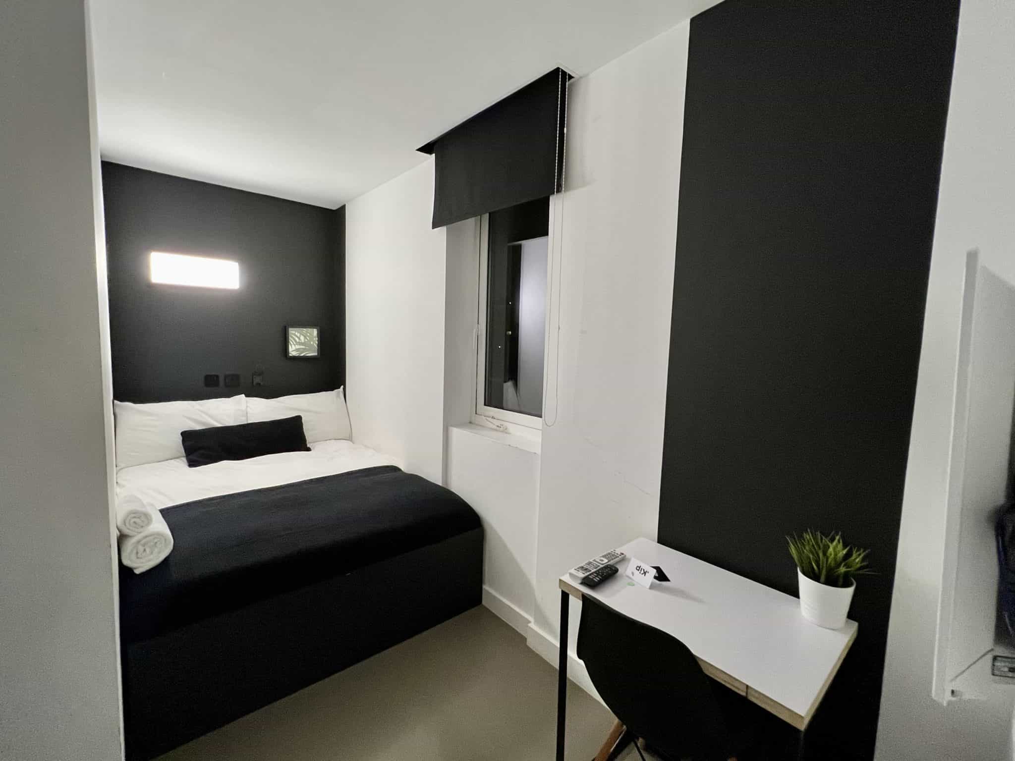 A double bed in a narrow room, decorated with black and white furnishings