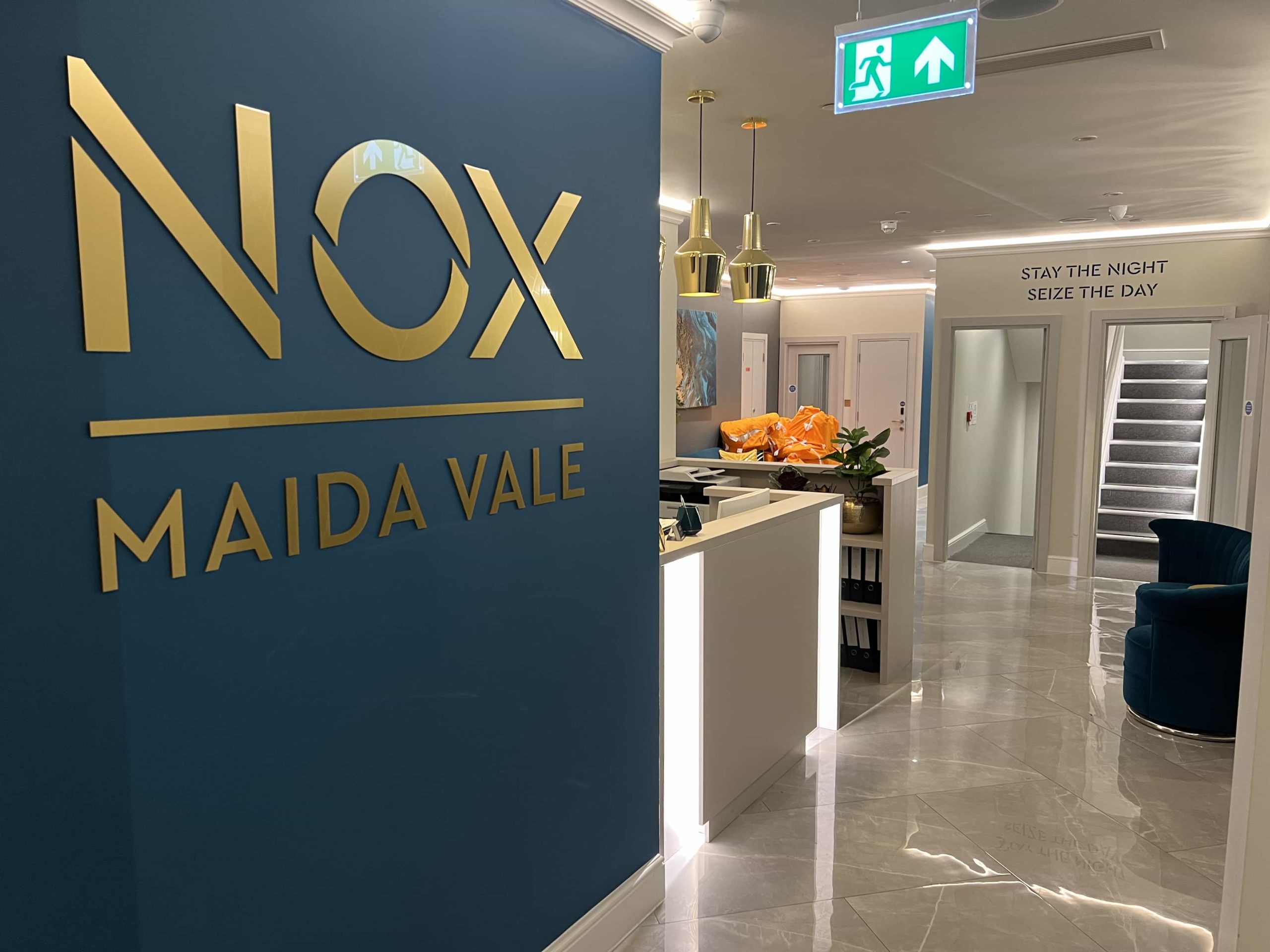 A large NOX, Maida Vale logo on the left, with the reception desk of the hotel lobby to the right