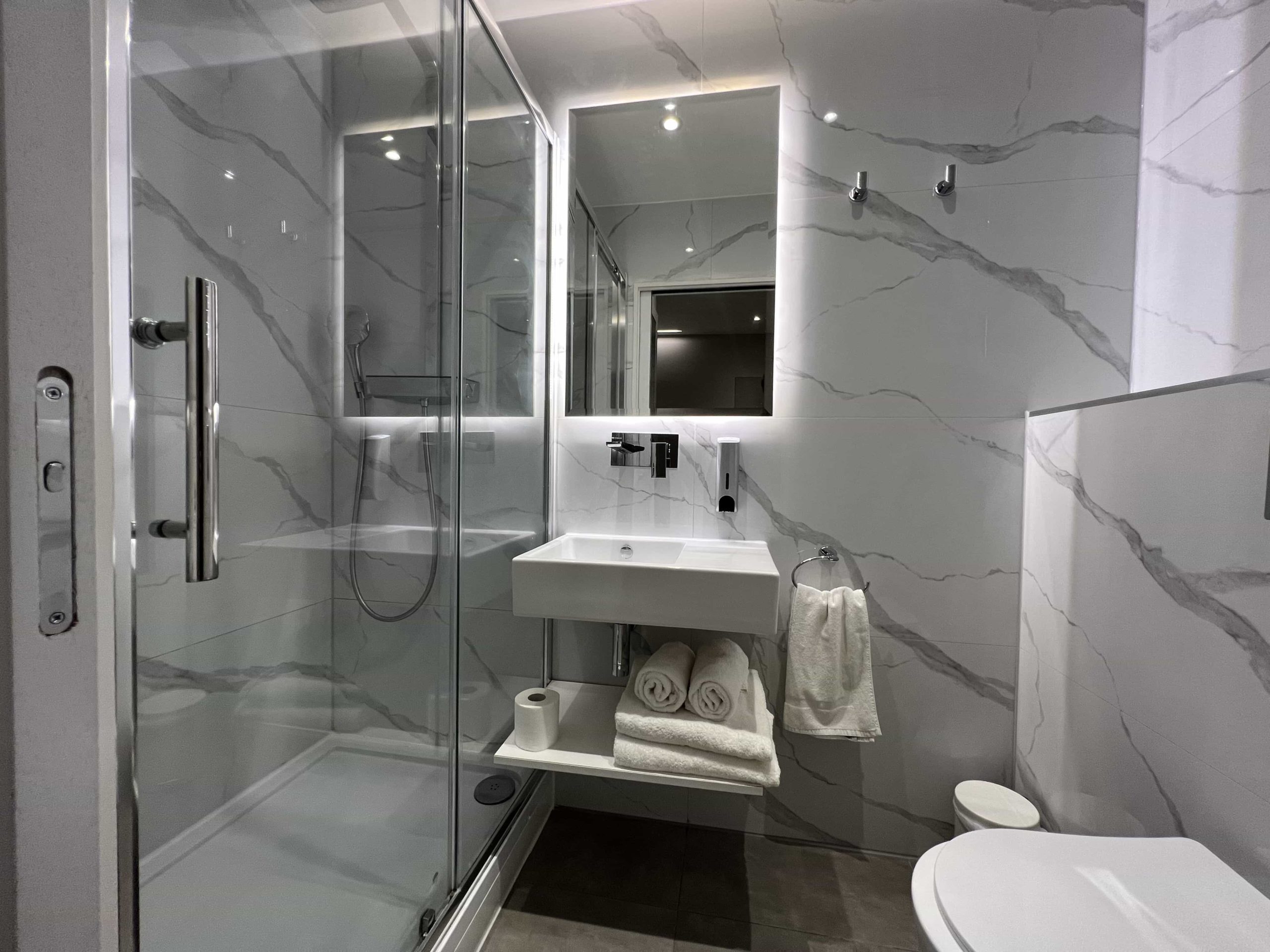 A brightly-lit bathroom with a walk-in shower, decorated with marble-effect tiles