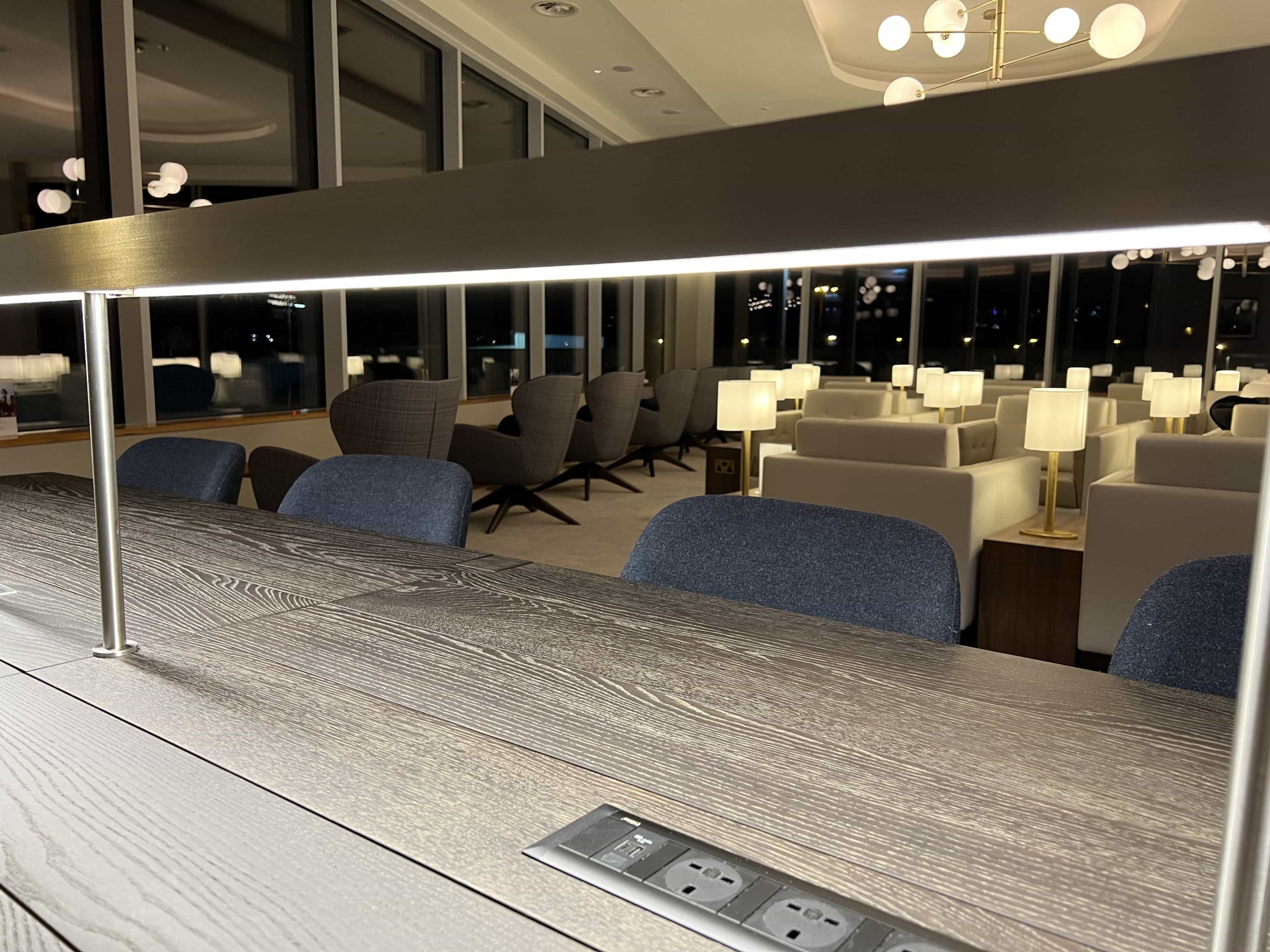 A workstation area illuminated by integrated strip lighting, situated in the corner of an airport lounge