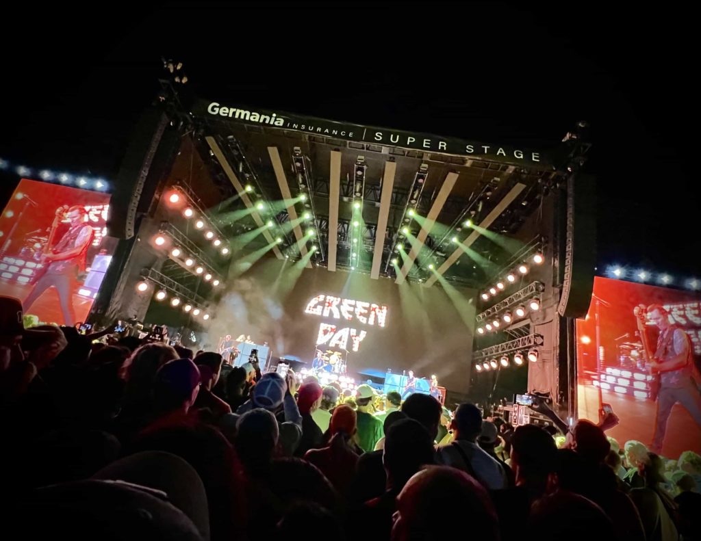 Green Day performing on a large stage, with screens at either side