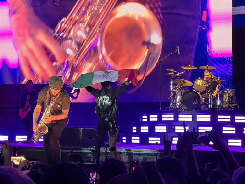 Billie Joe Armstrong from Green Day holding a Mexican flag while another band member plays a saxophone solo