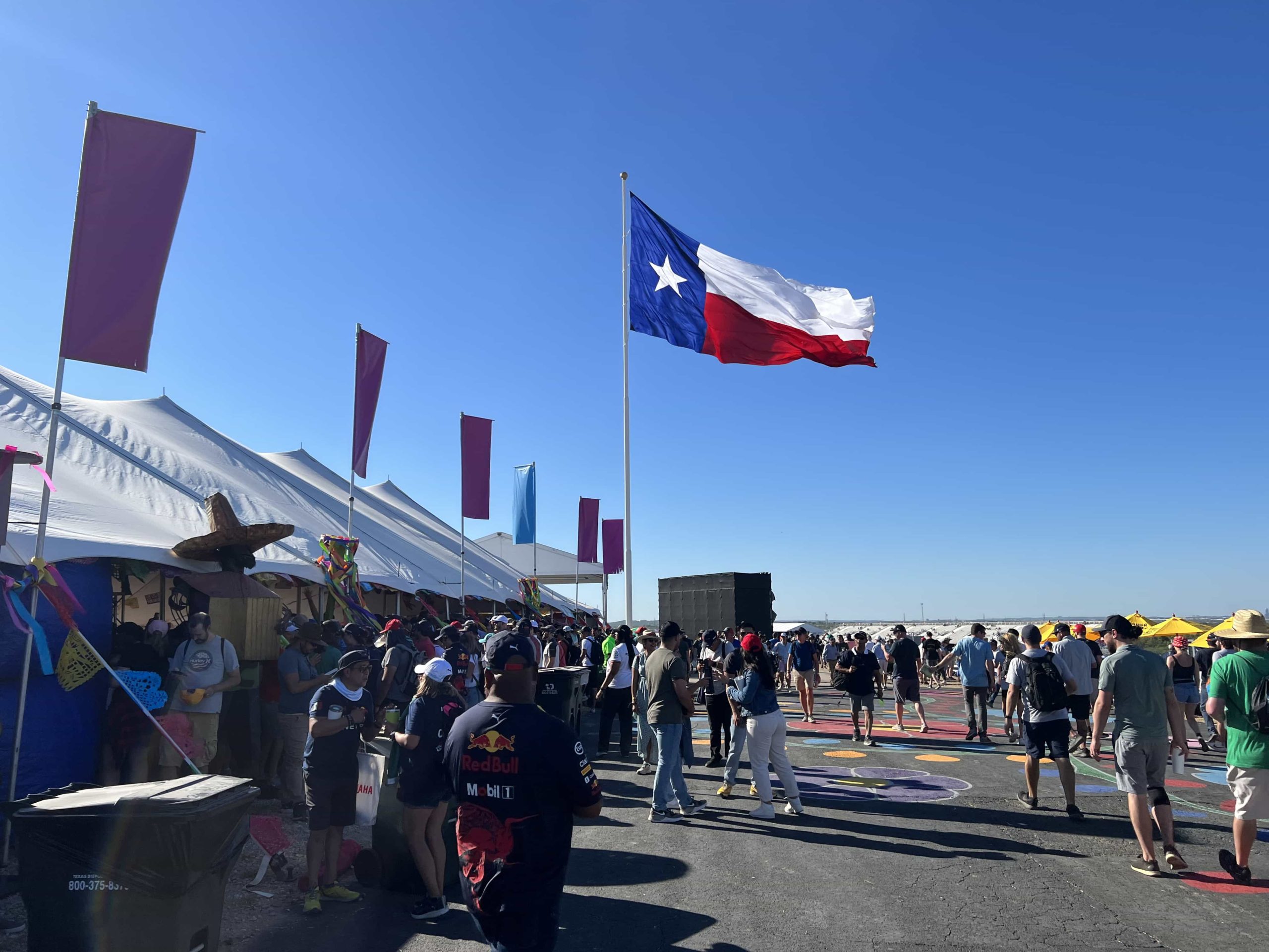 A crowd of F1 fans in front of a food village, with a giant Texan flag in the background