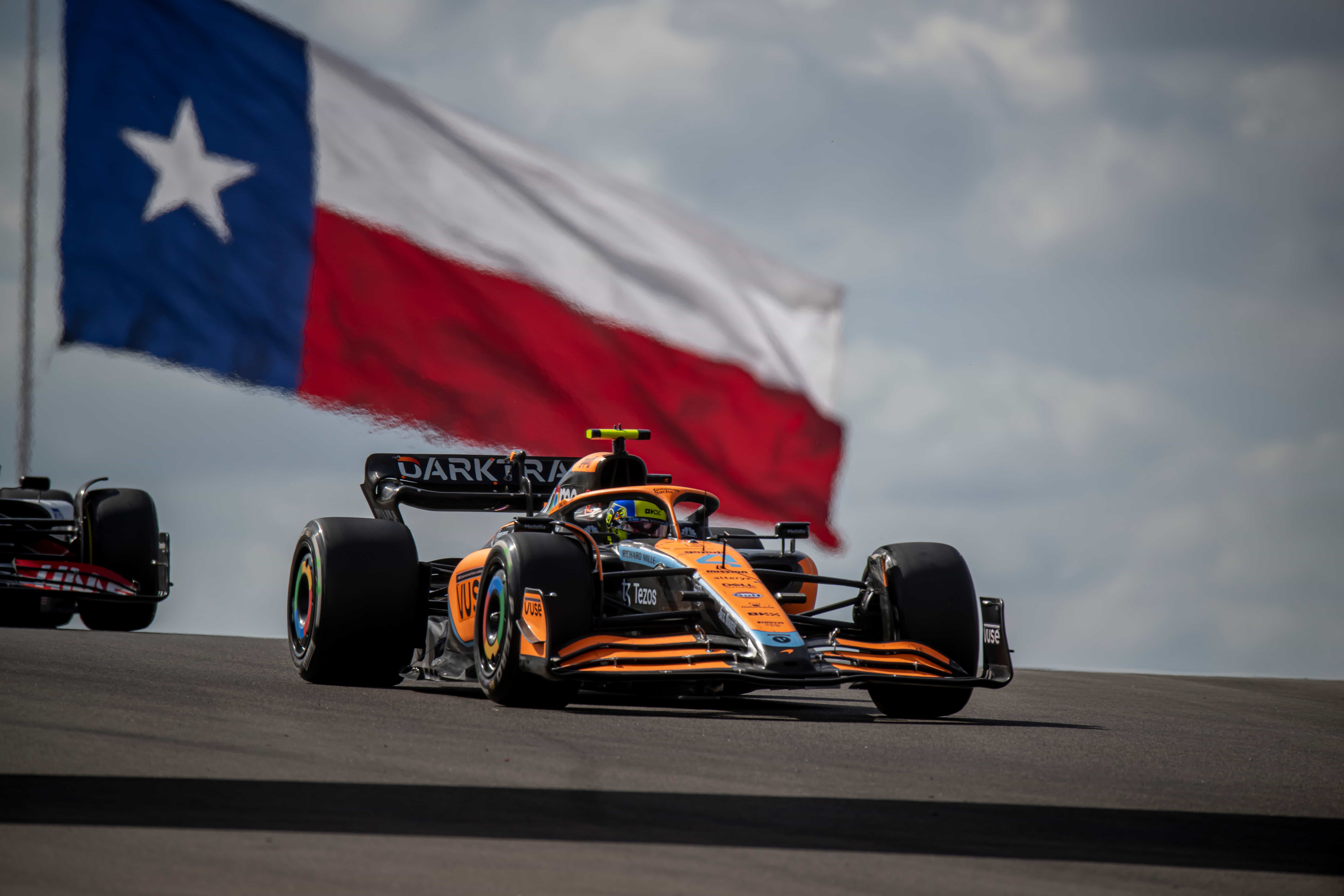 A McLaren F1 car during a race, with a giant Texan flag in the background