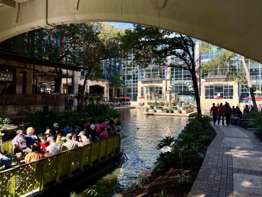 A stretch of the San Antonio riverwalk, taken from underneath a bridge beneath which a boat is passing through