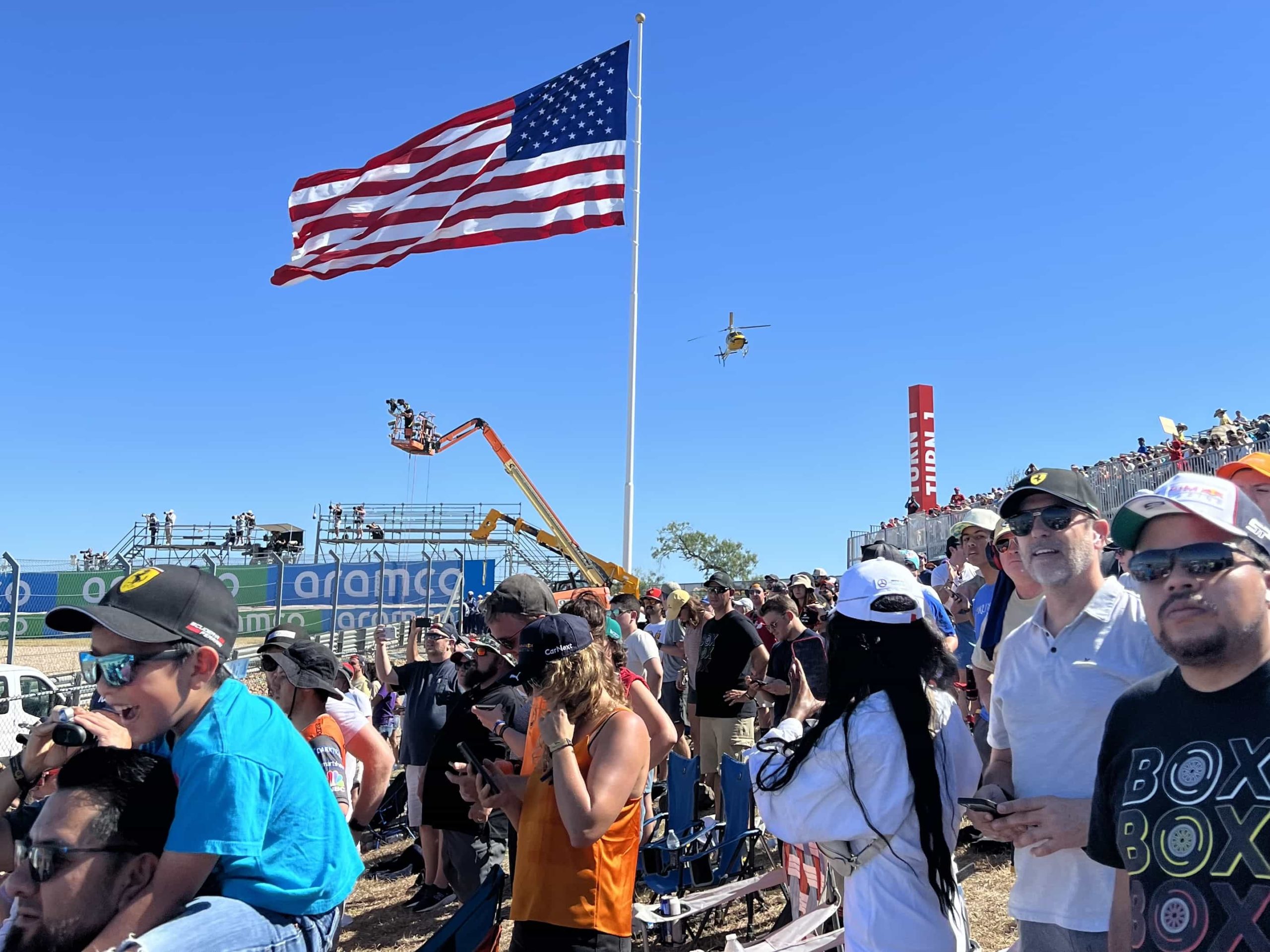 F1 fans watching a race, with a giant American flag in the background