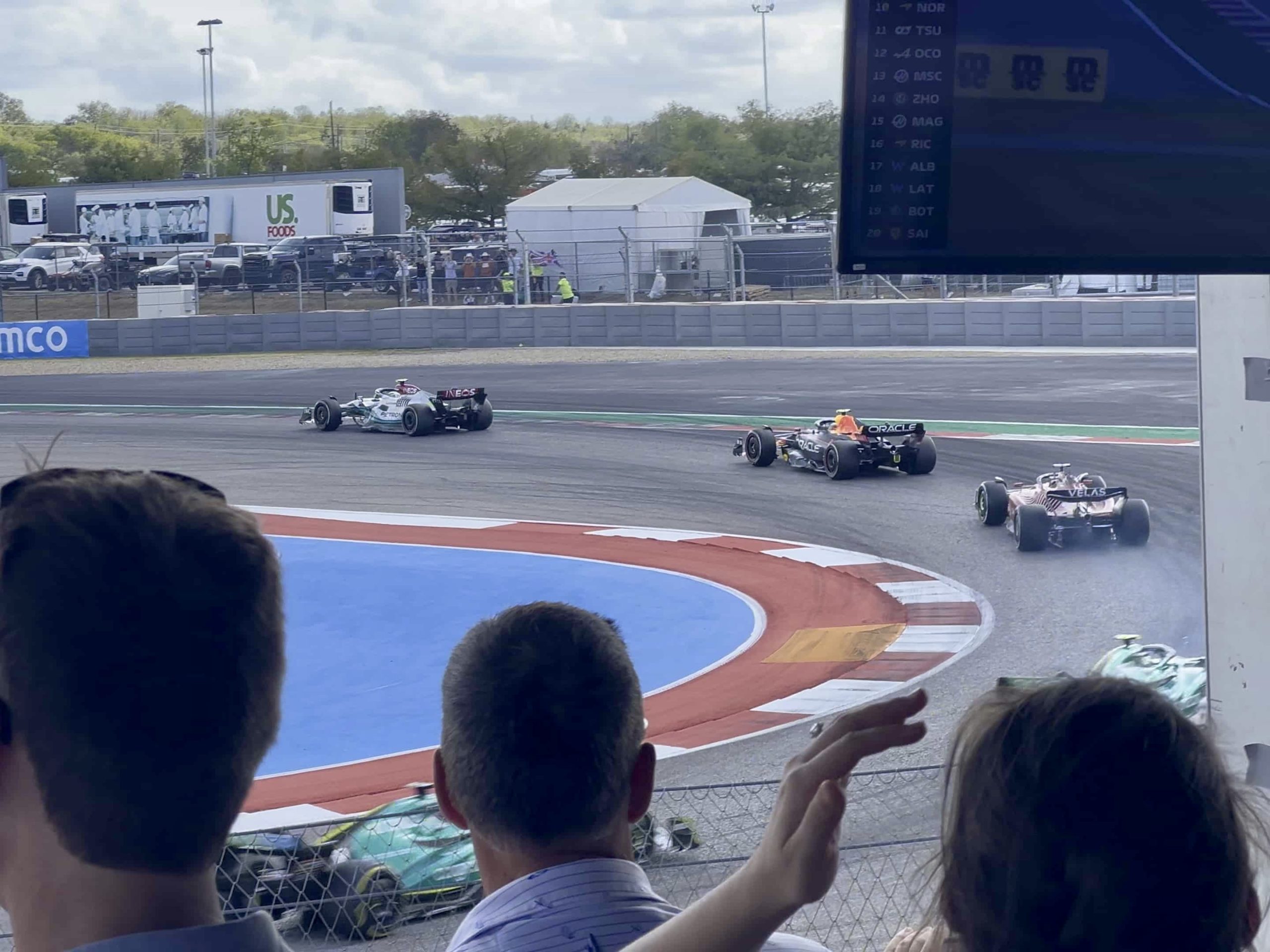 Five F1 cars in close succession through Turn 20 at COTA, watched by a crowd from a grandstand