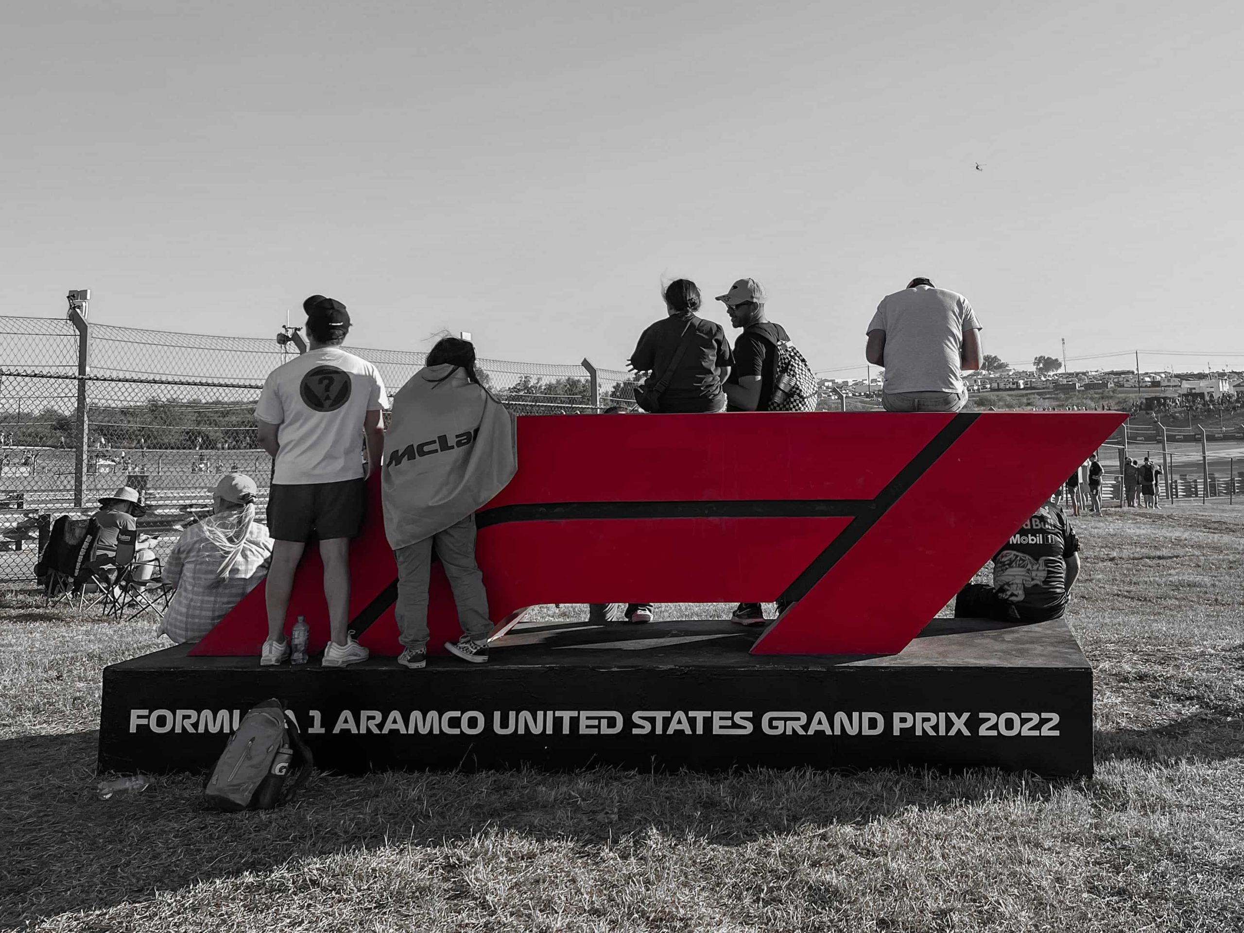 a 3D version of the F1 logo in a grassy area with fans standing and sitting on it
