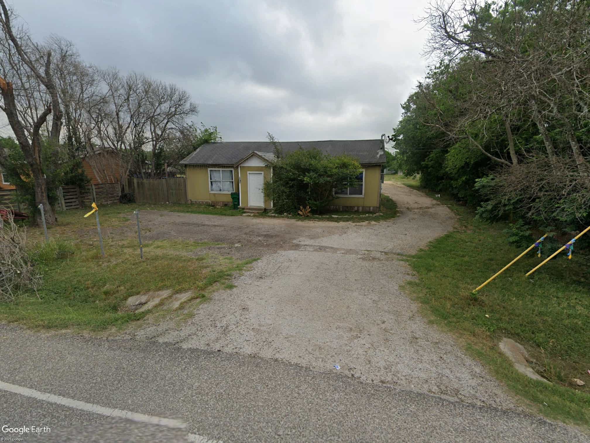 A yellow house, with a driveway down the side, leading to some derelict land which is used for parking during race events