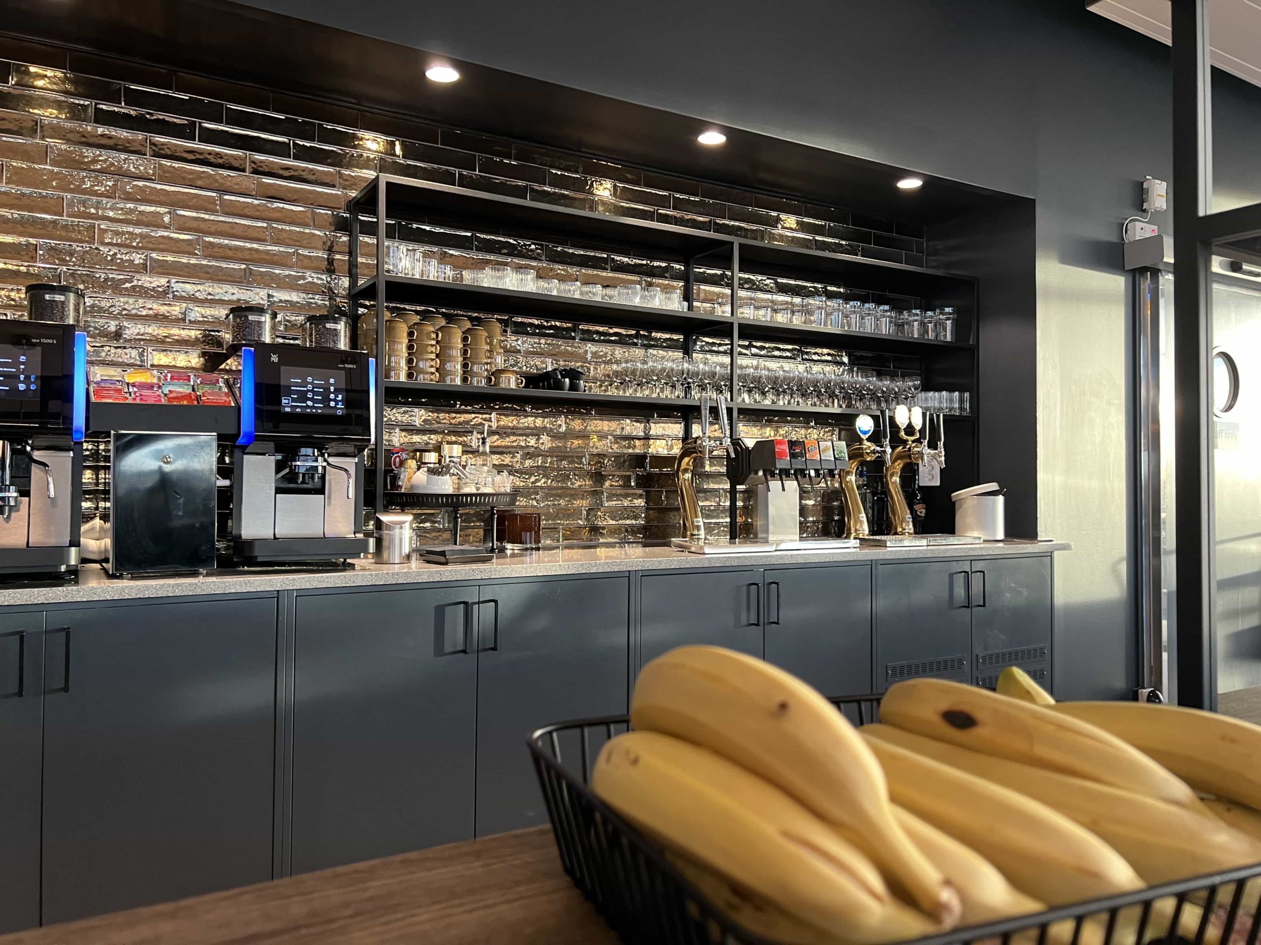 Coffee machines, next to a selection of drinks on tap, with glassware and mugs on shelves above