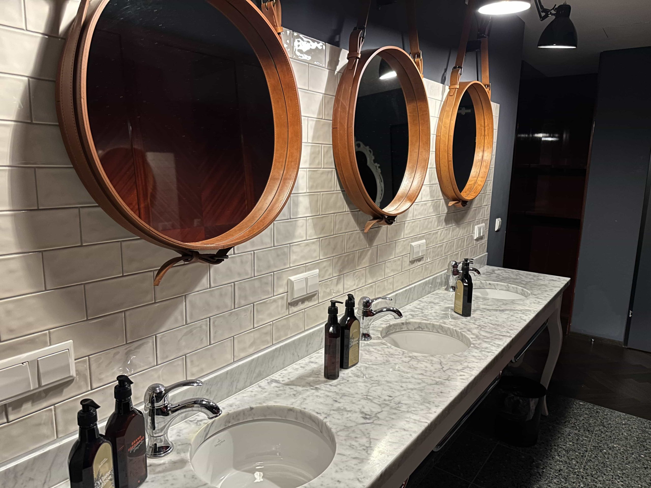 Three communal sinks, each with soaps, mirrors, and trash bins