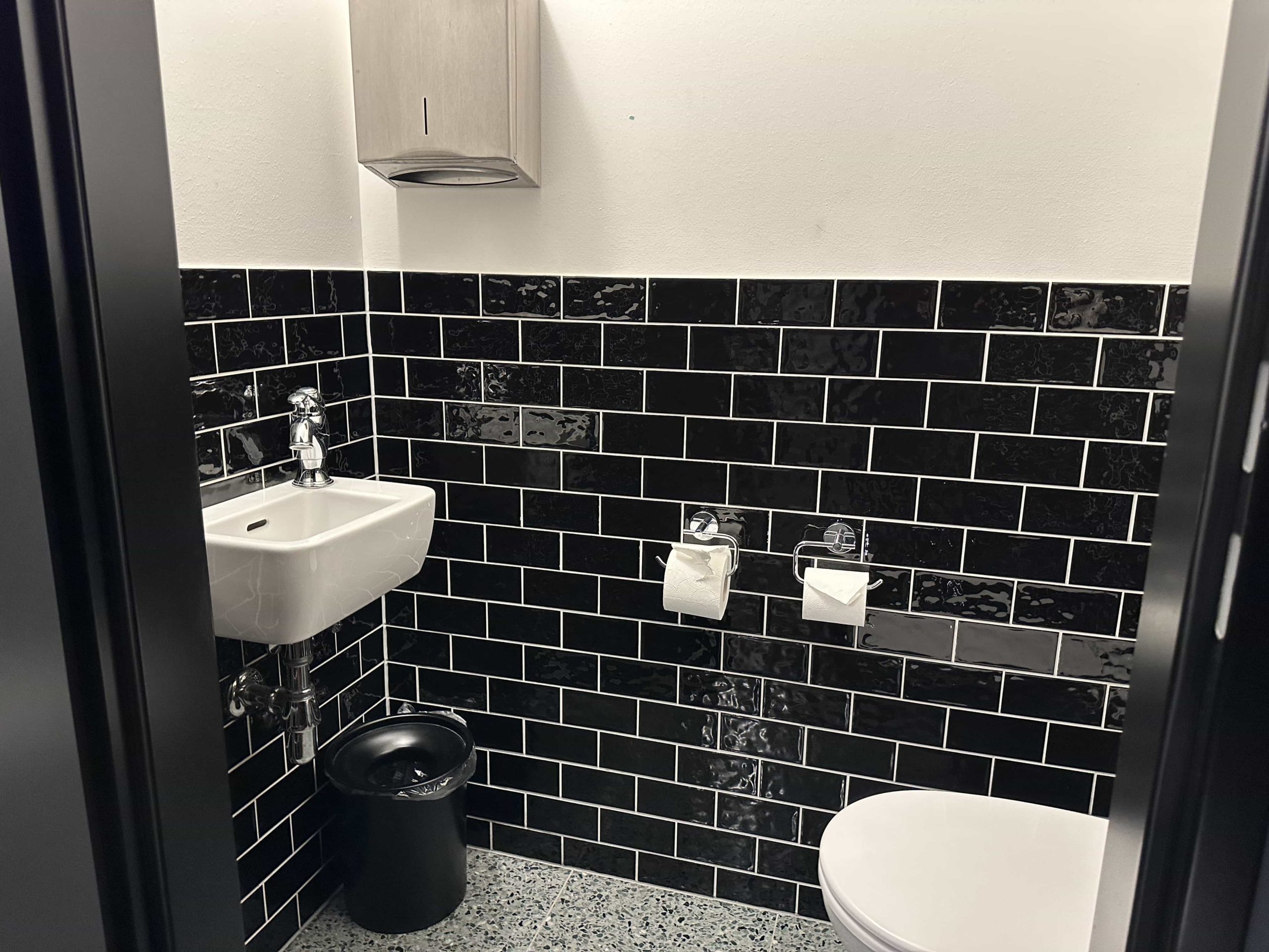 A toilet room (WC), with a toilet, small sink, and paper towel dispenser 