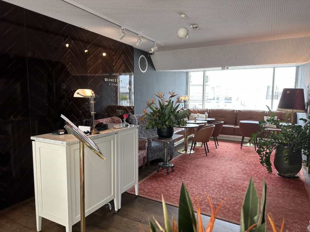 A reception desk within a hotel restaurant, with tables and seats in the background