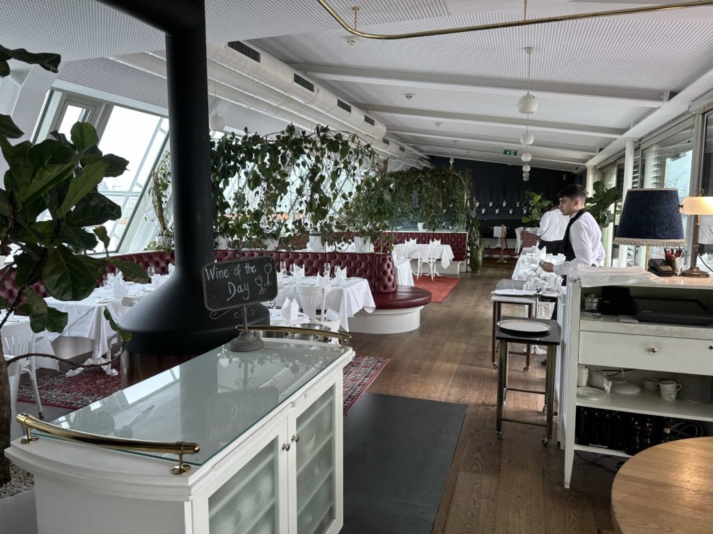 Formal seating within a rooftop hotel restaurant, with views on either side of the room over the city