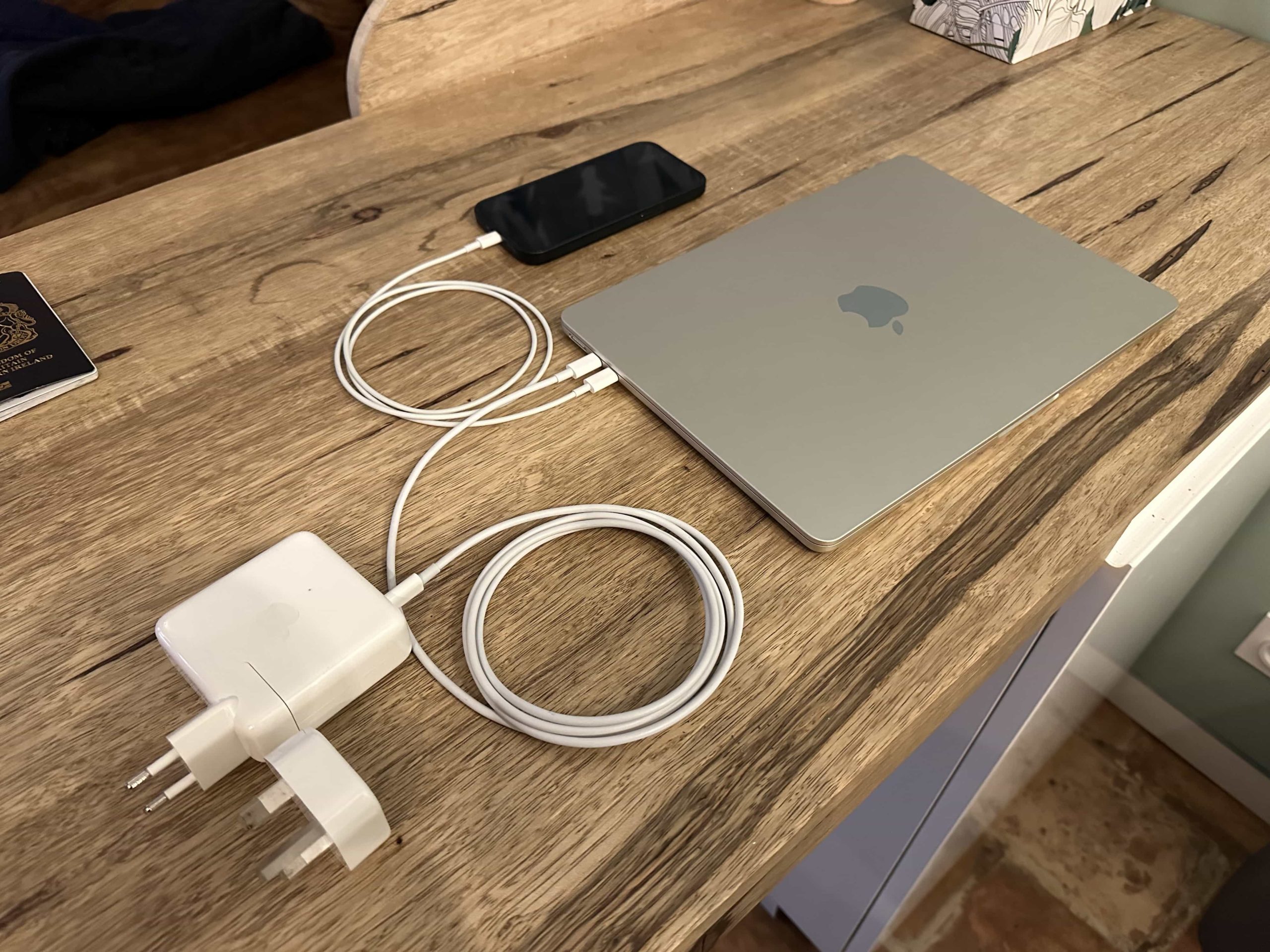 A MacBook, charging cables and adapters, and a phone atop a kitchen countertop