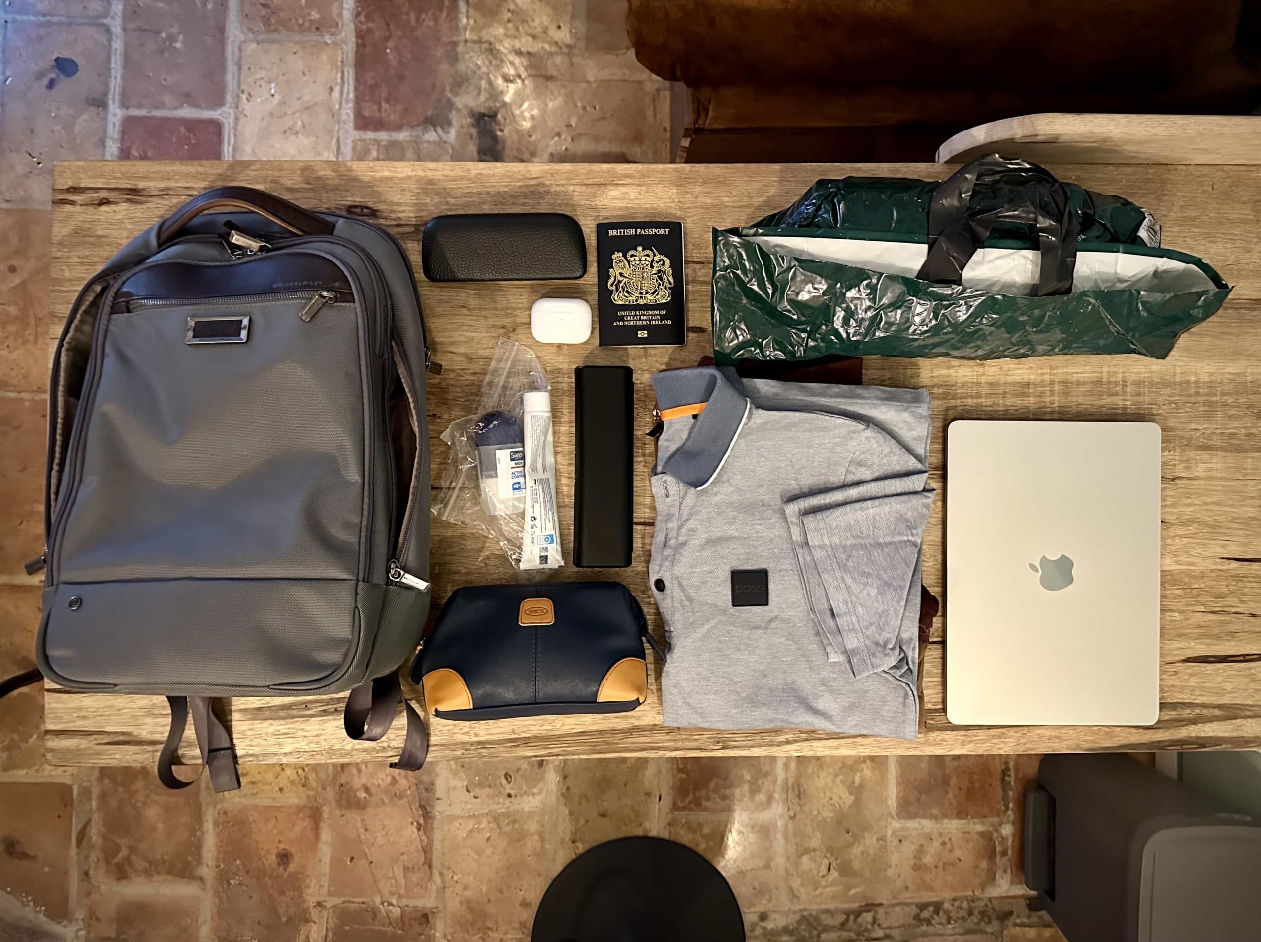 A top-down view over a backpack sitting along side its extracted contents, including clothing, devices, and toiletries