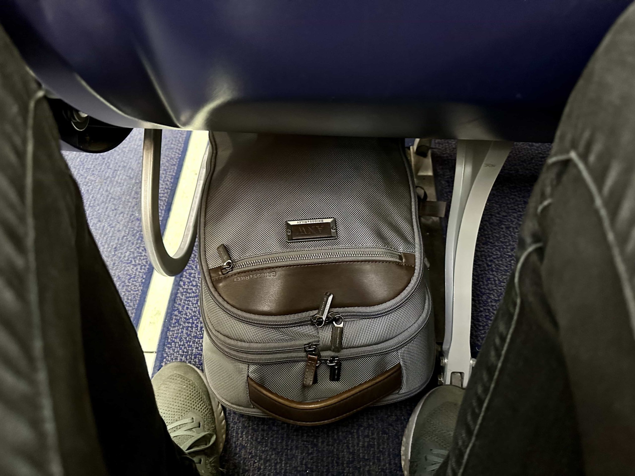 A backpack slotted underneath an economy-class plane seat