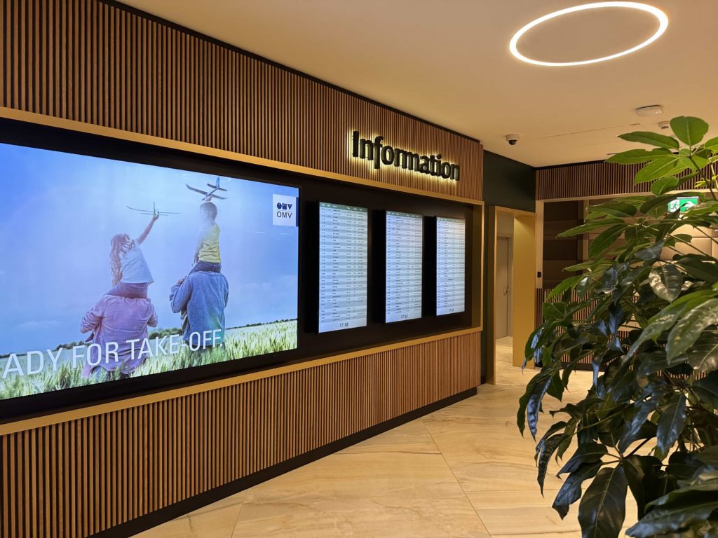 A large advertisement board, with flight departure screens to the right, under an 'Information' sign