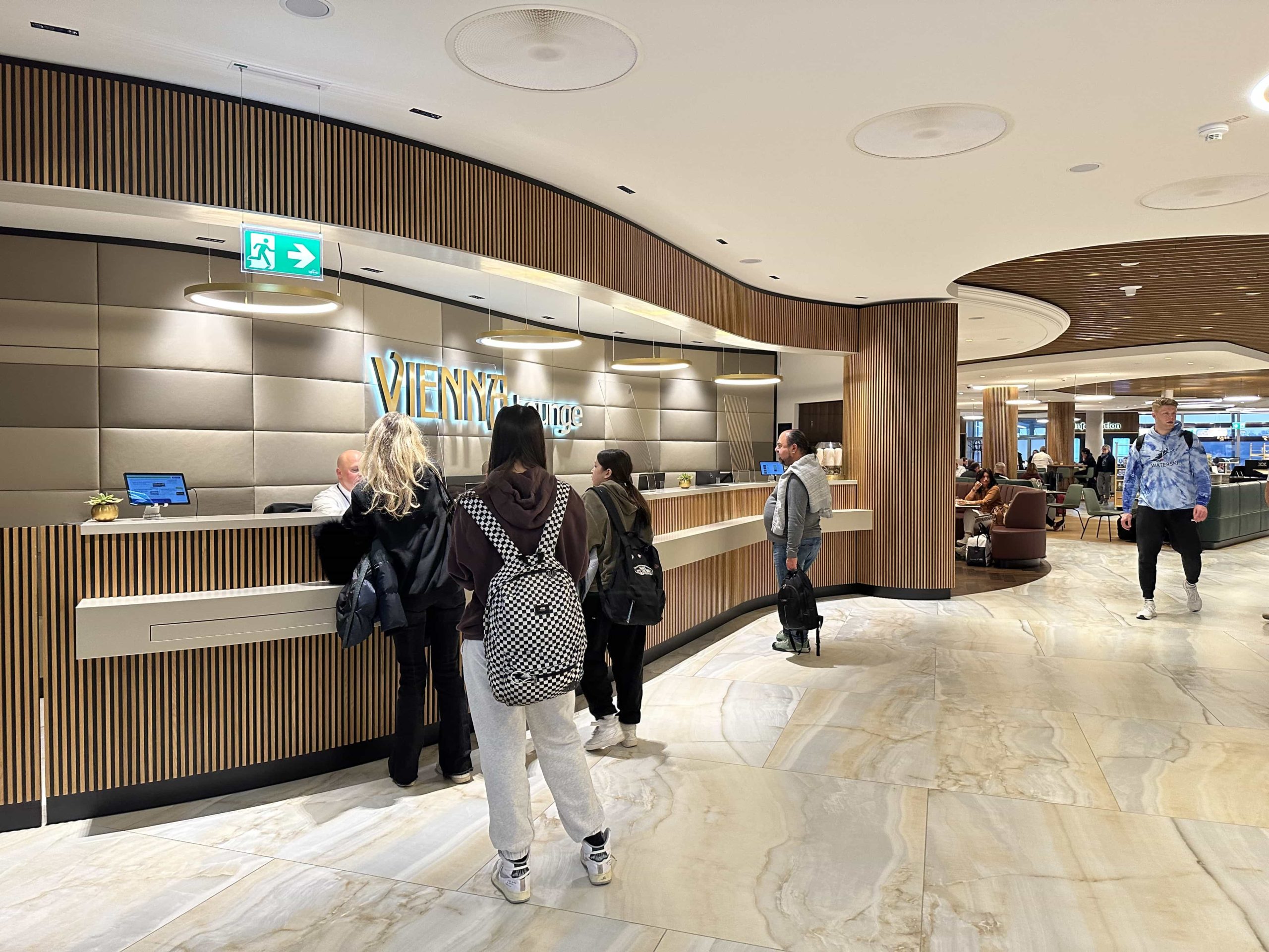 A reception desk, with a queue of people checking in to an airport lounge