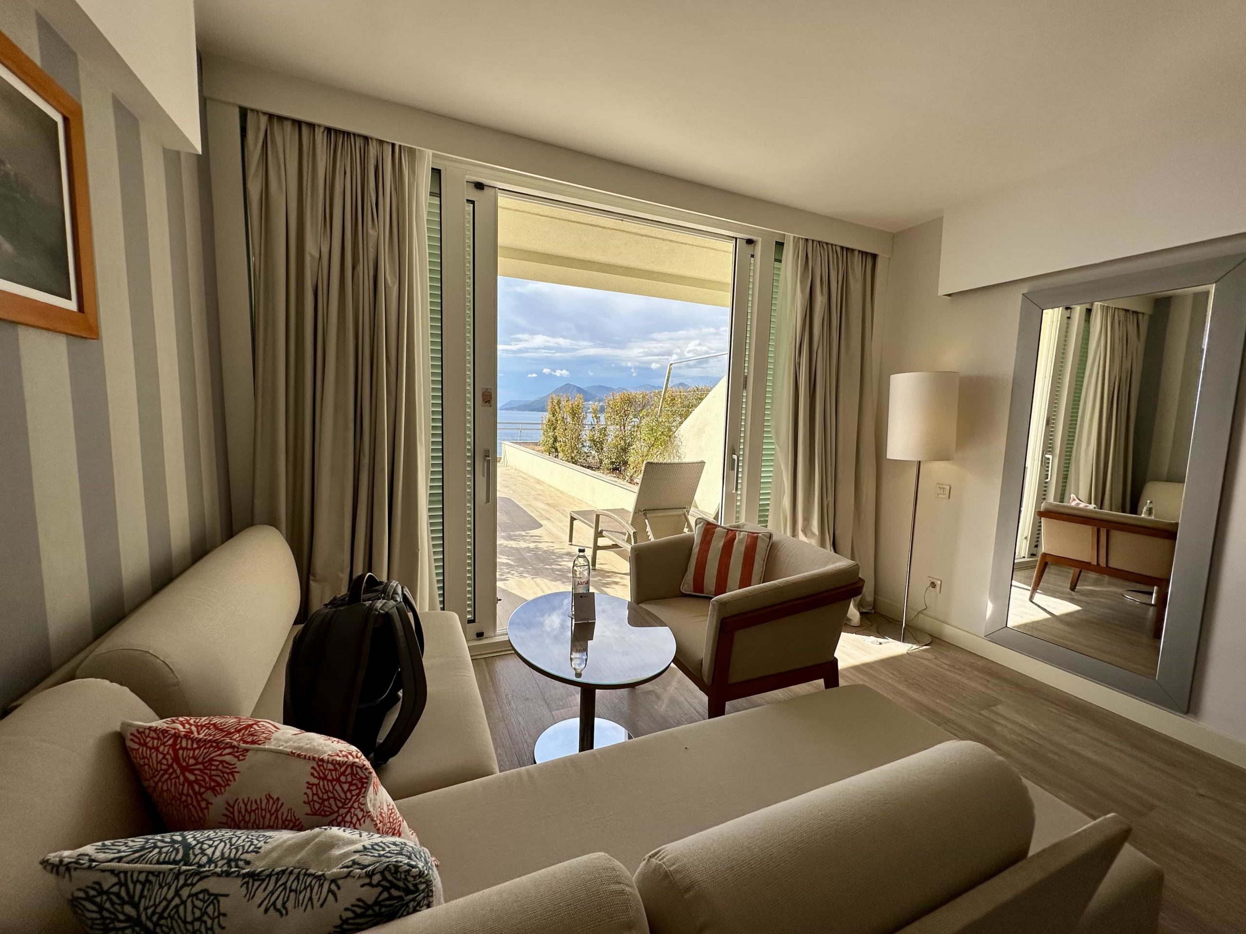 A living area in a hotel room, comprised of a corner sofa, a table and a lounge chair