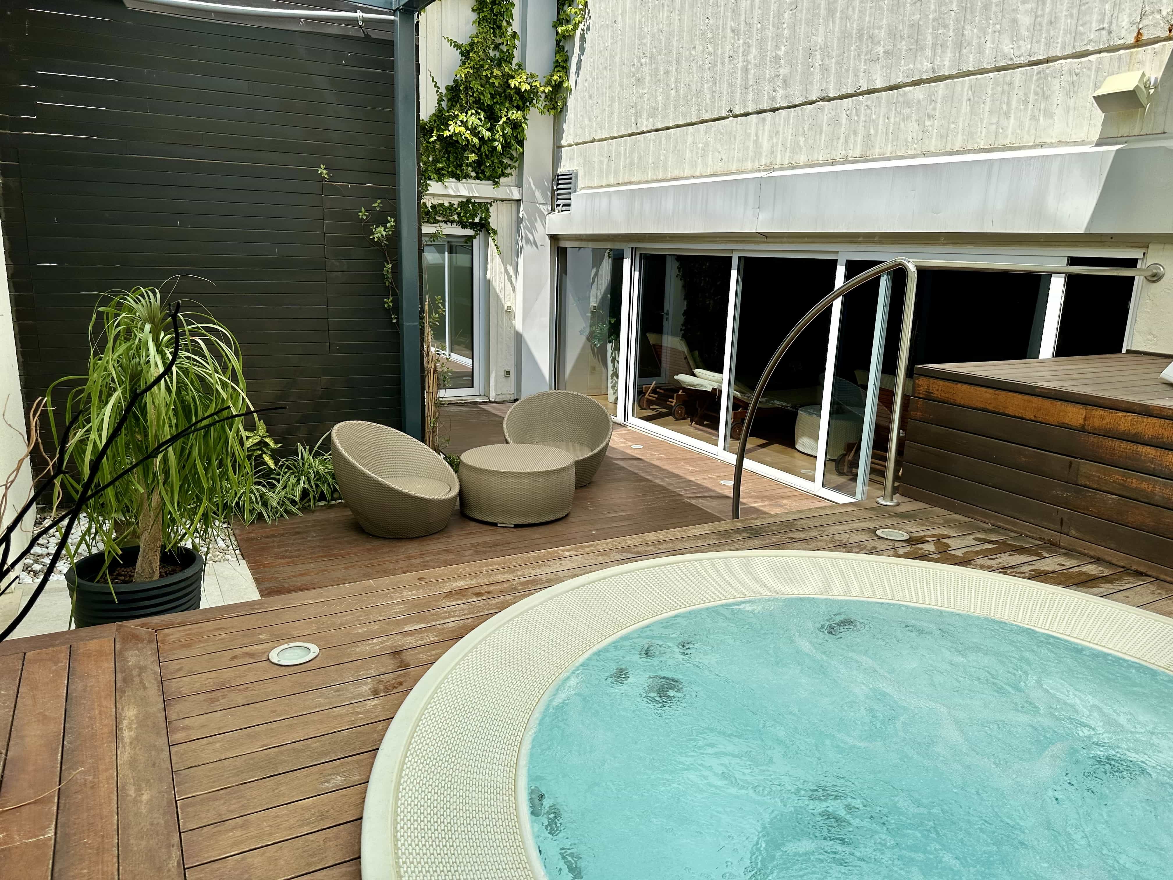 A small jacuzzi in a covered outdoor space, with planters and seating nearby