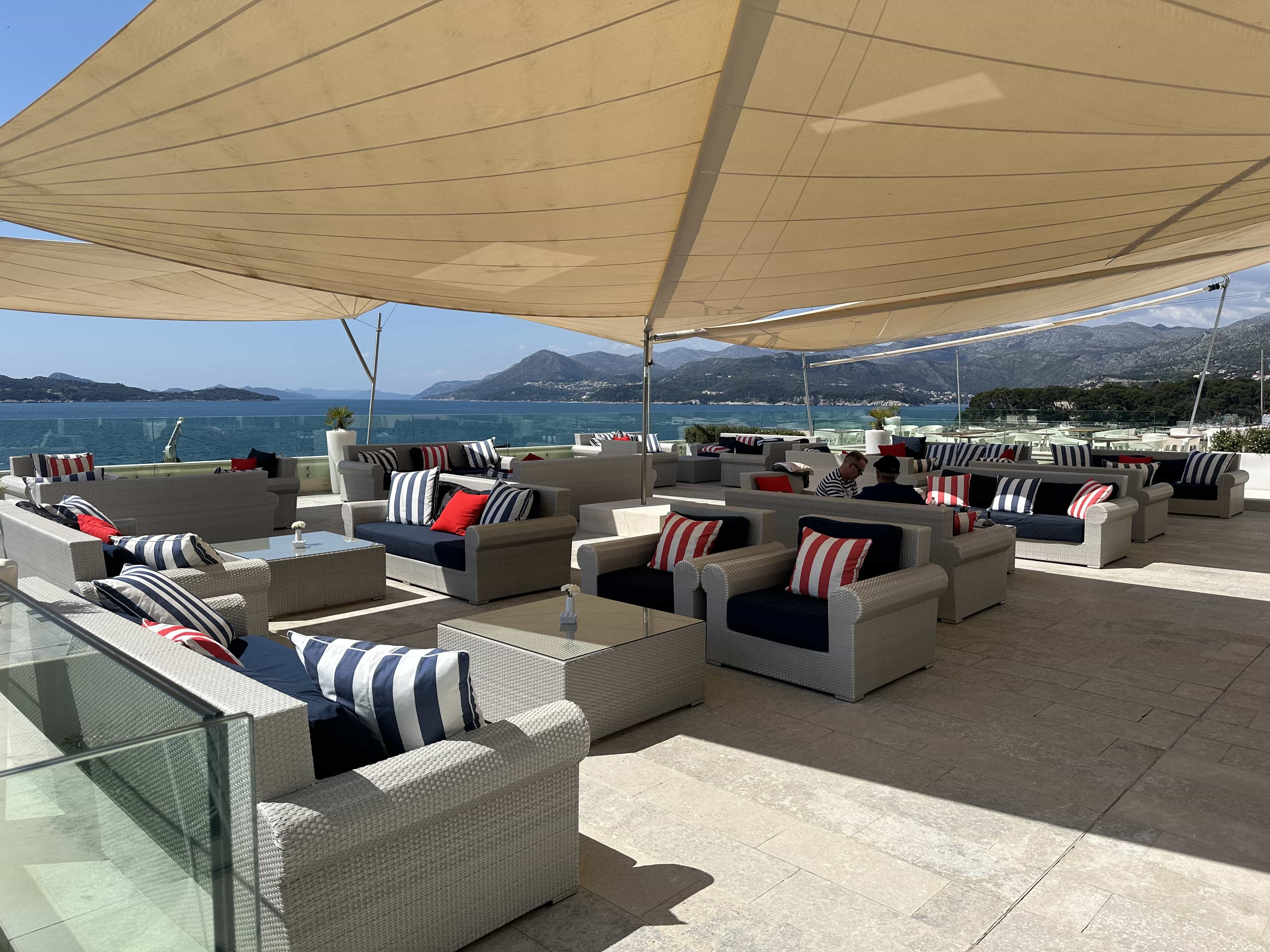 Casual lounge-style seating in a shaded outdoor bar area, with panoramic views over the sea