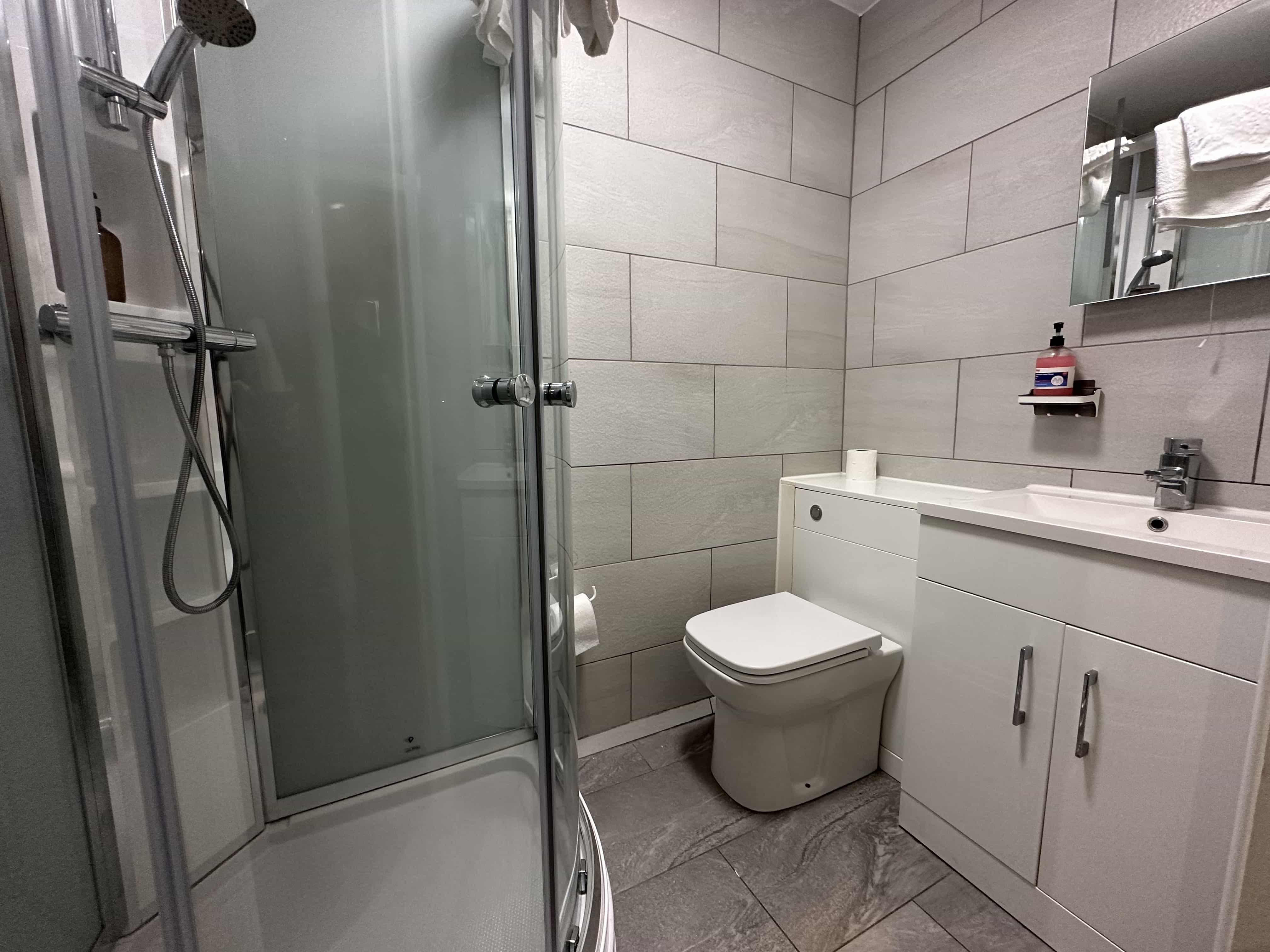 A modern bathroom with a corner shower, toilet, sink unit