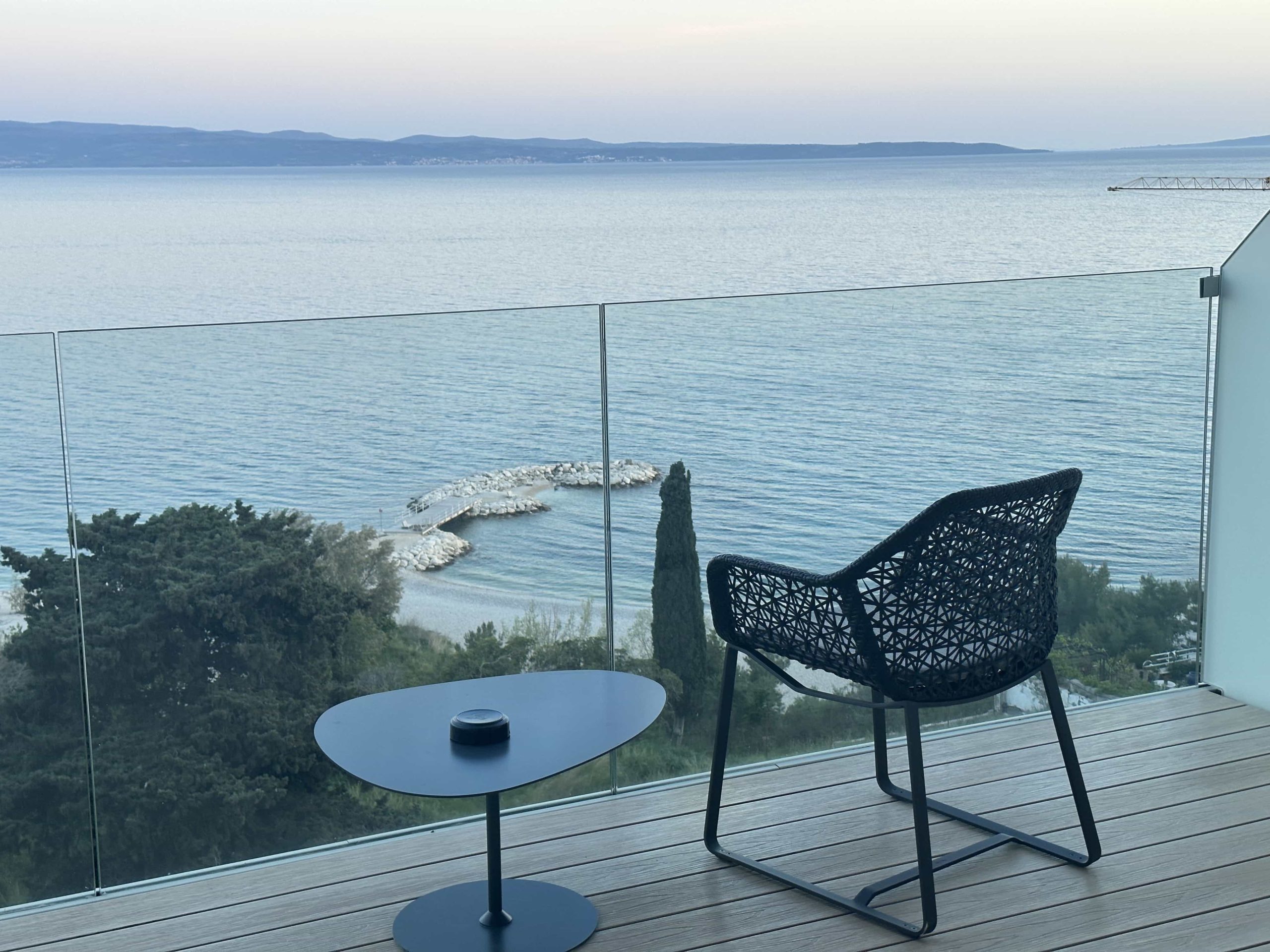 A chair and a side table on a hotel balcony, with views out to the sea