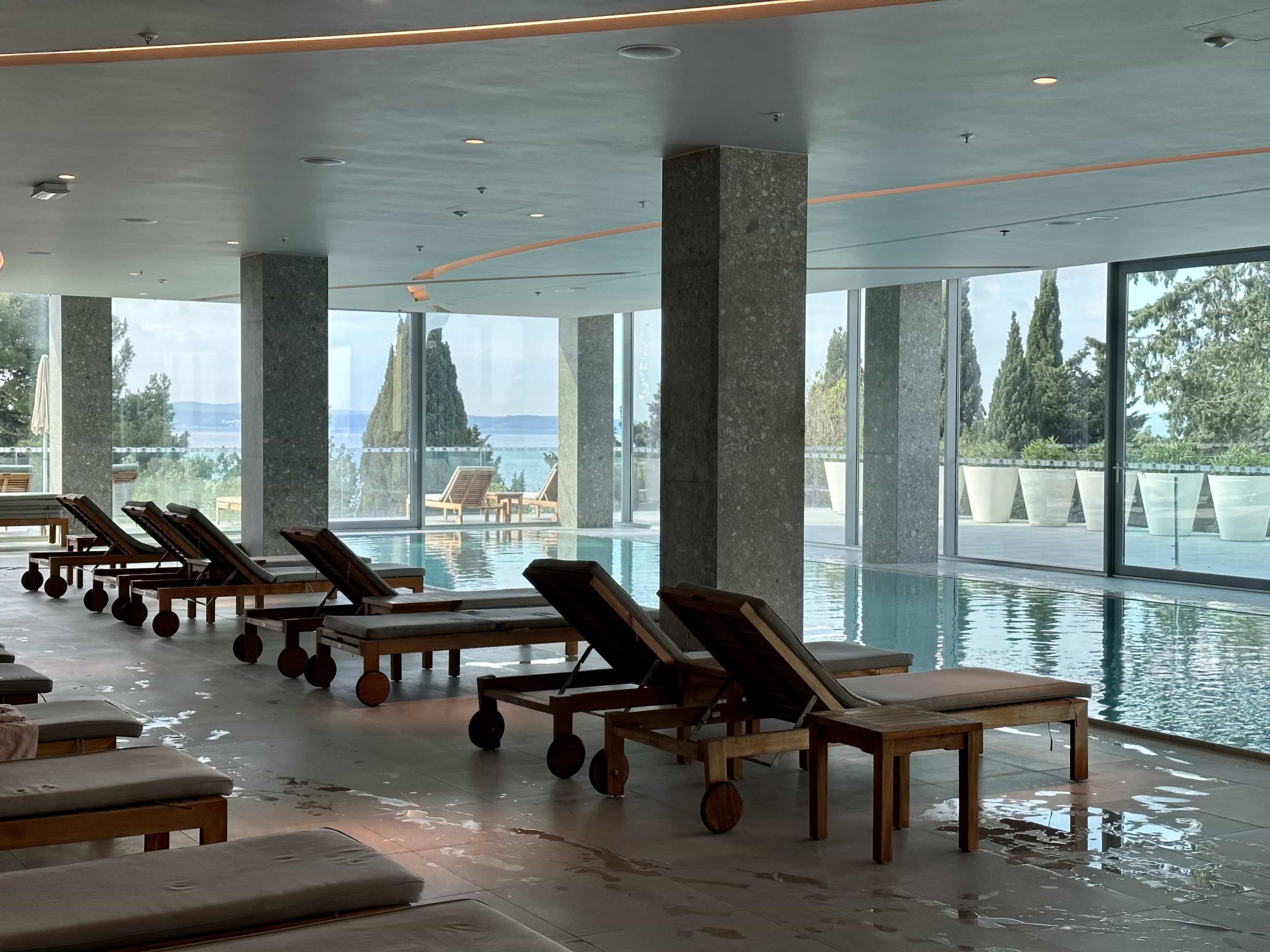 A line of loungers, beside the edge of an indoor pool within a hotel spa