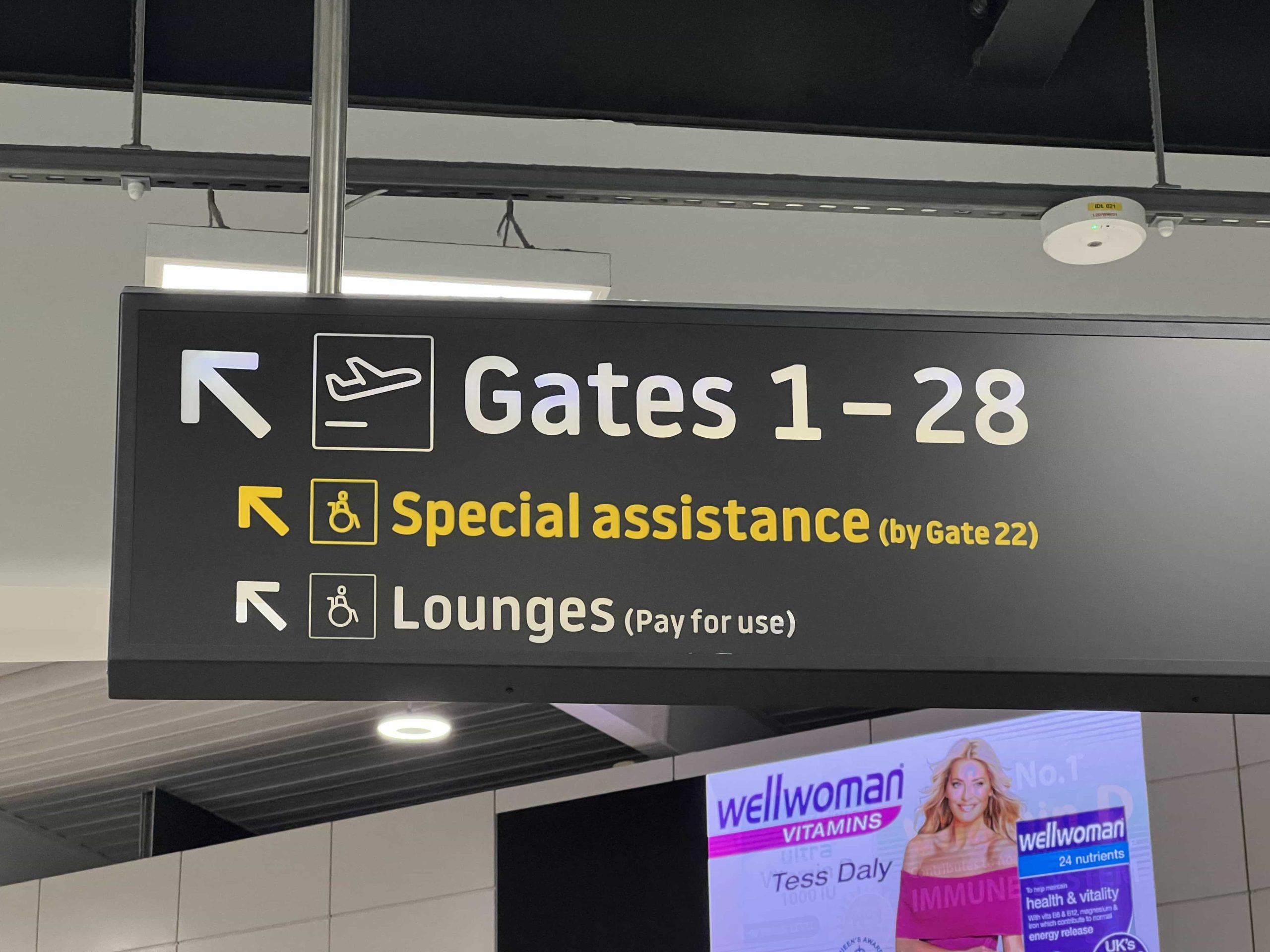 Overhead signage in an airport terminal which directs to gates, special assistance, and lounges