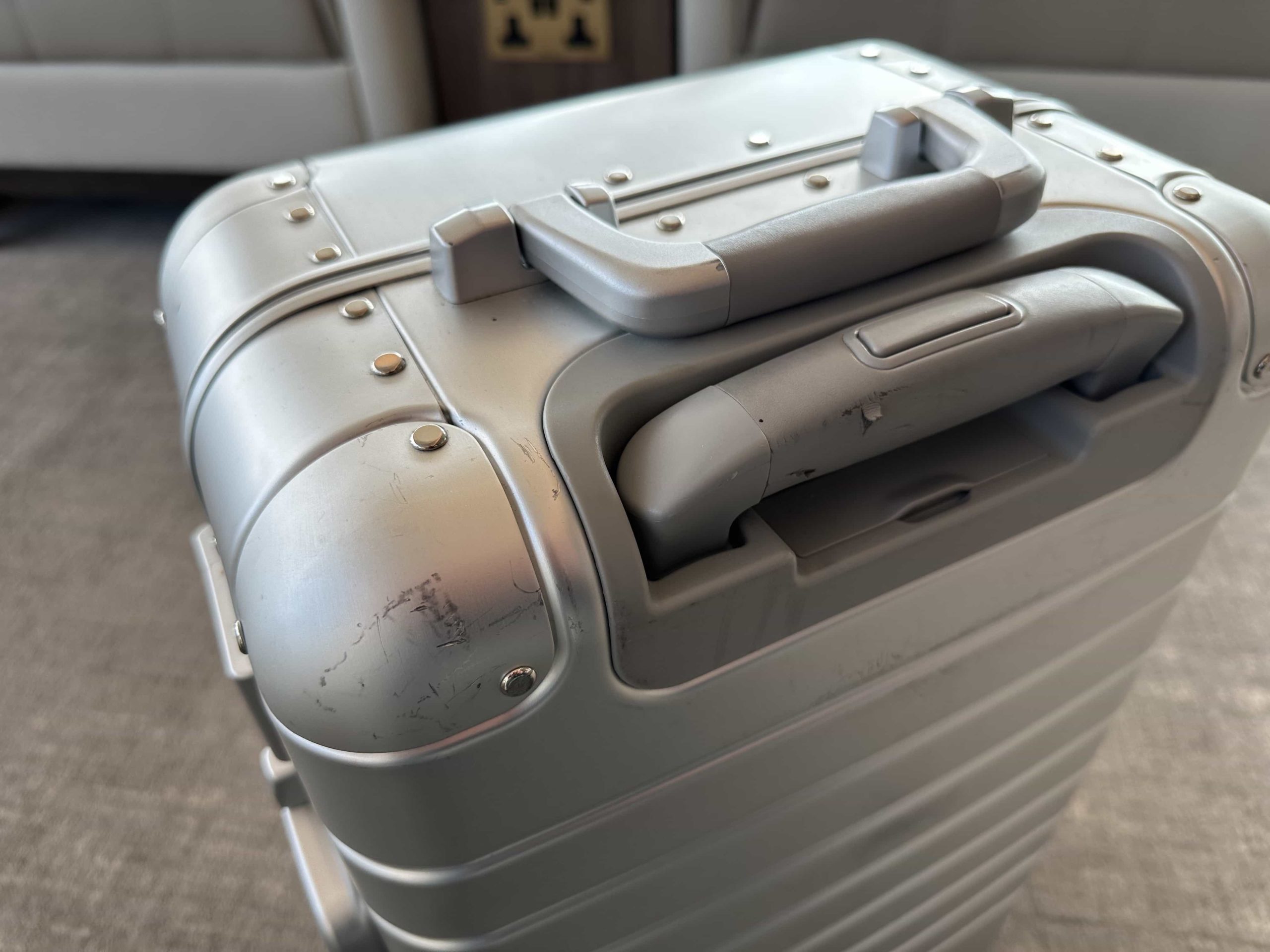 A suitcase positioned to highlight scuffs and scratches on the corners and wear on the handle