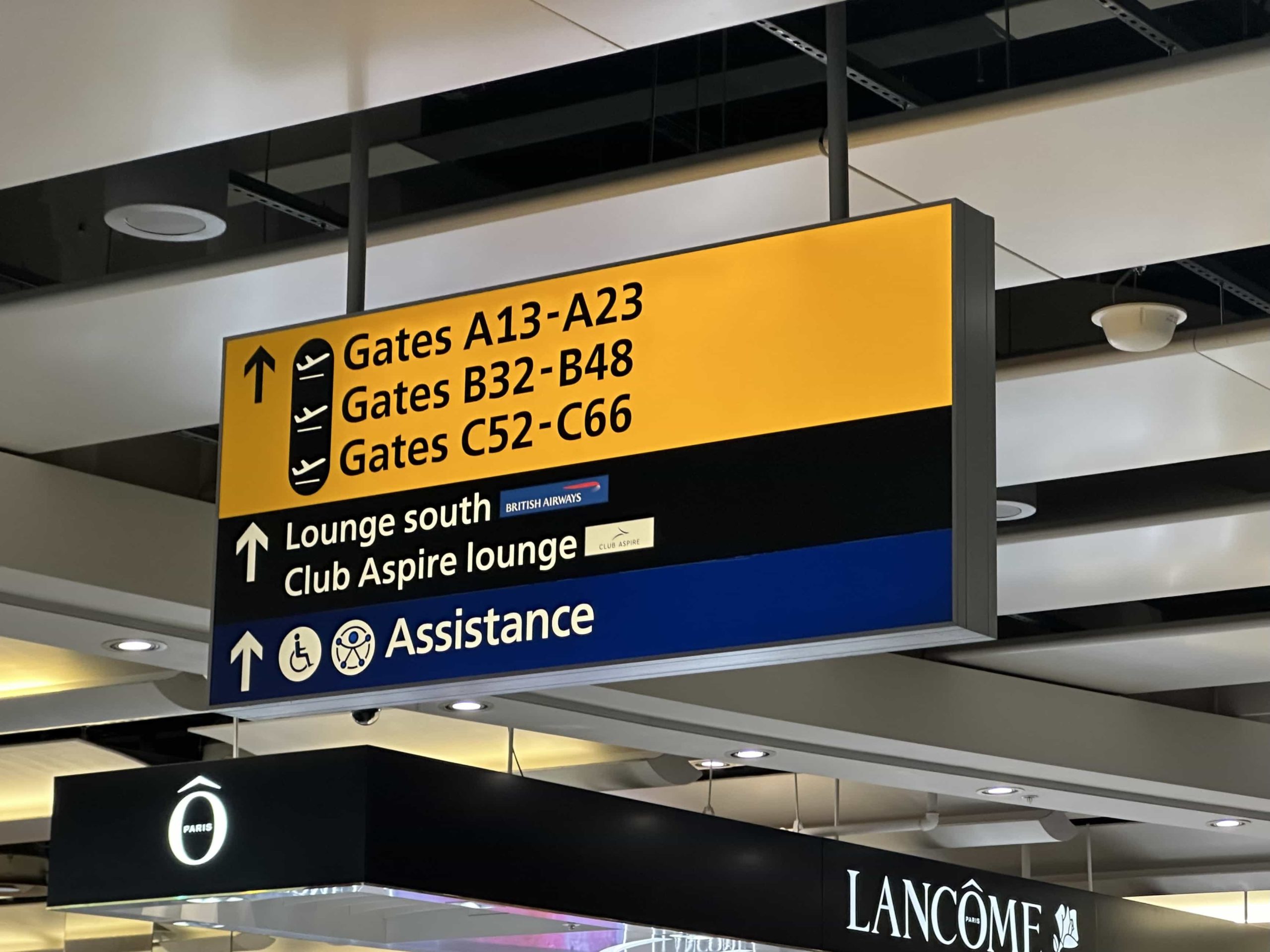Overhead signage in an airport terminal directing to gates, lounges, and assistance