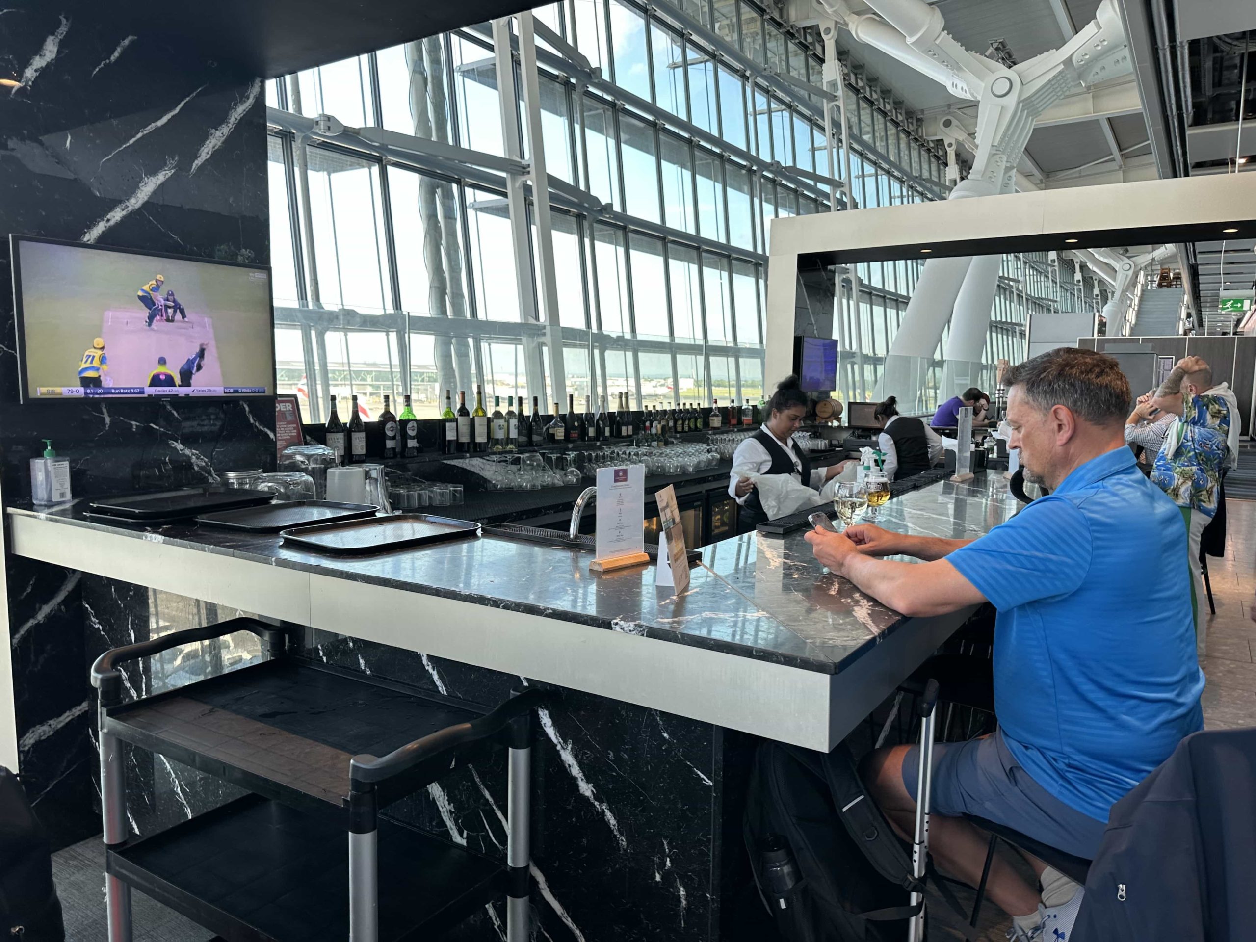 A bar in an airport lounge with bar stools, a TV, and a large selection of beverages
