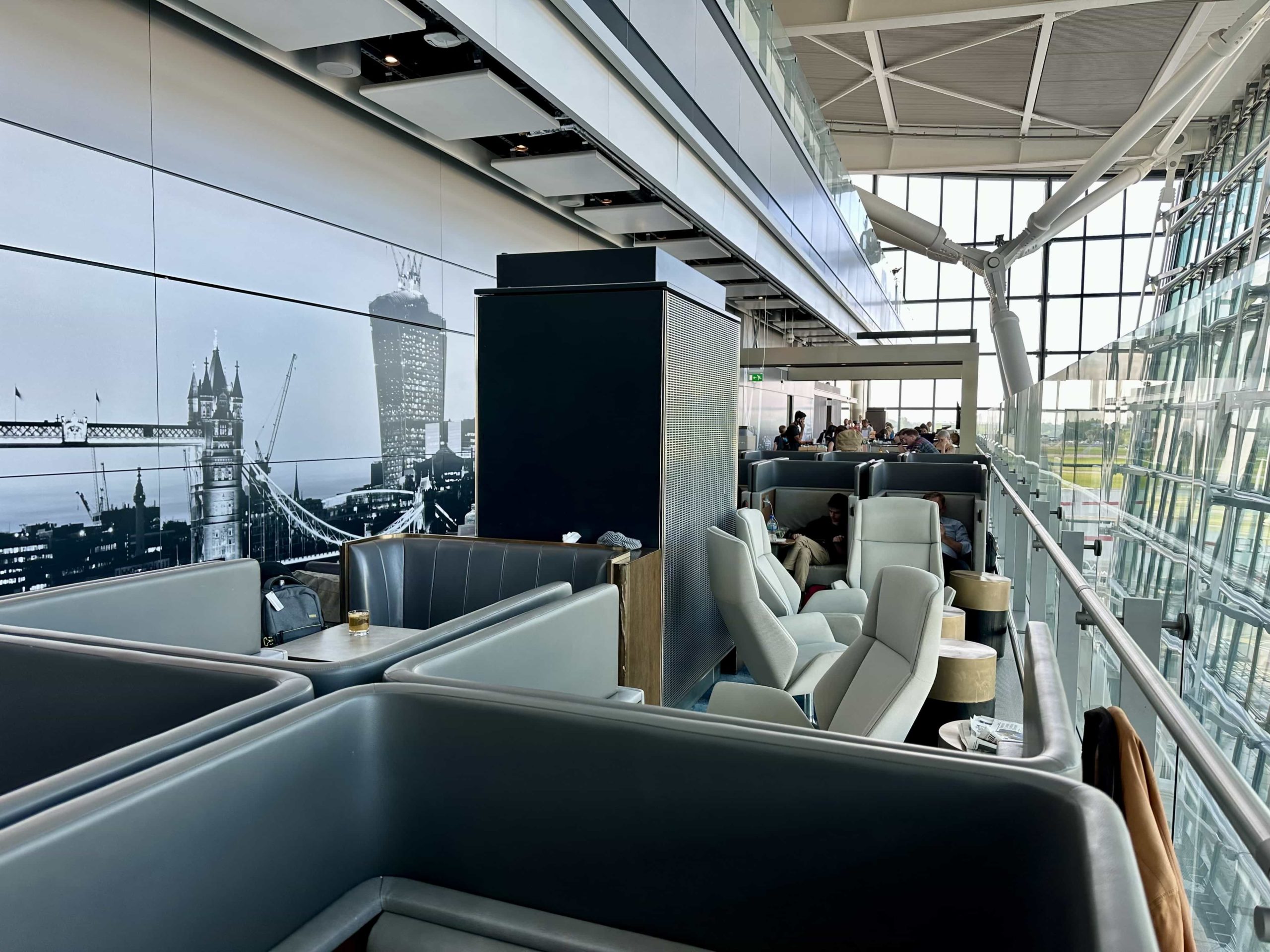 A long, narrow, open-air section of an airport lounge with a mixture of booth seating and armchairs
