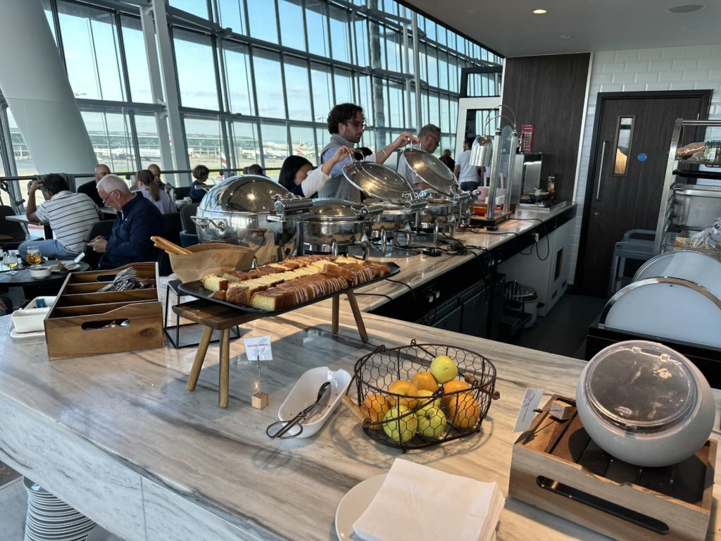 A selection of fruits, cakes, and hot dishes at an airport lounge buffet