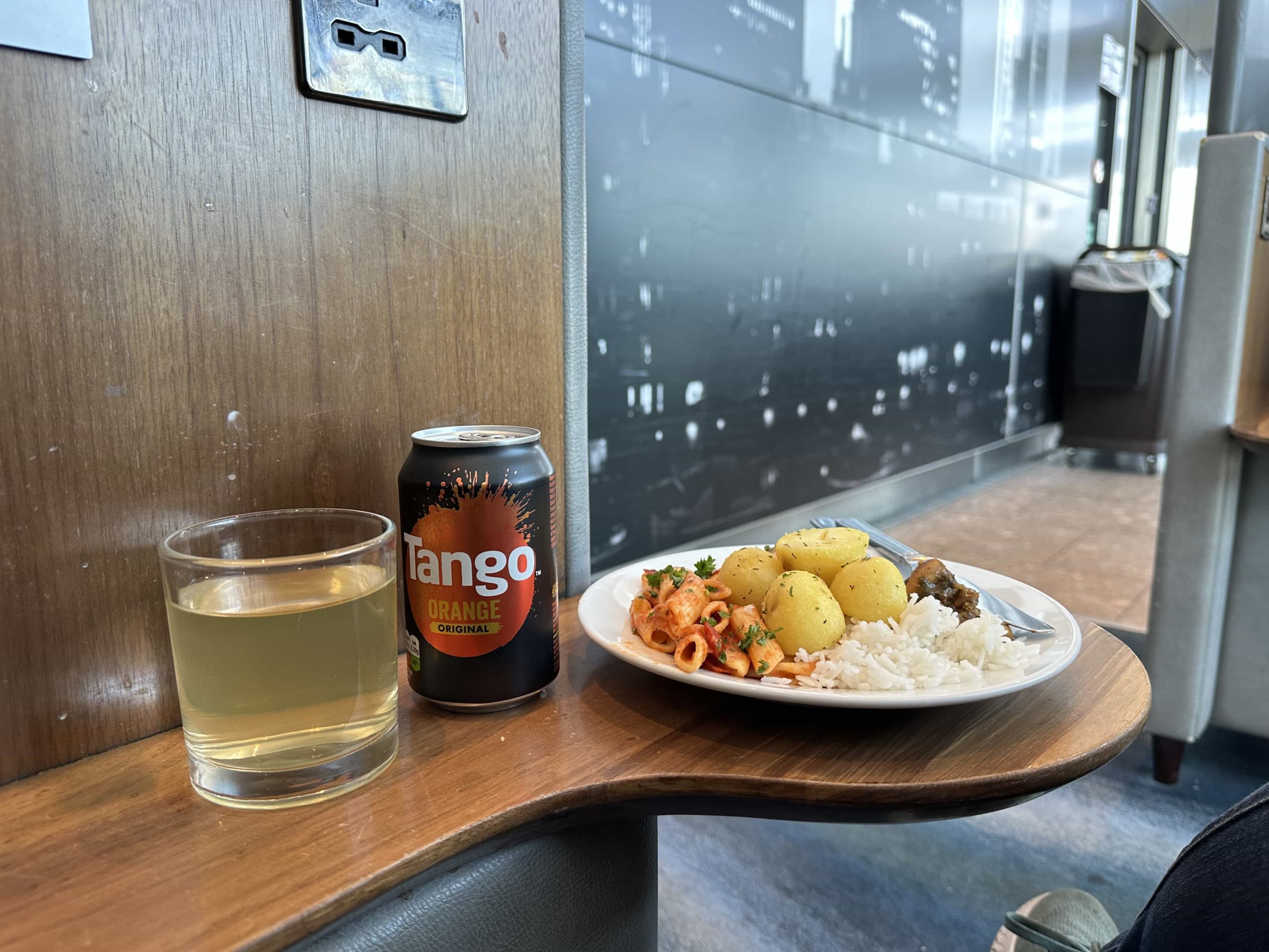 A fruit-infused water, a can of Tango, and a plate of curry, rice, pasta, and potatoes